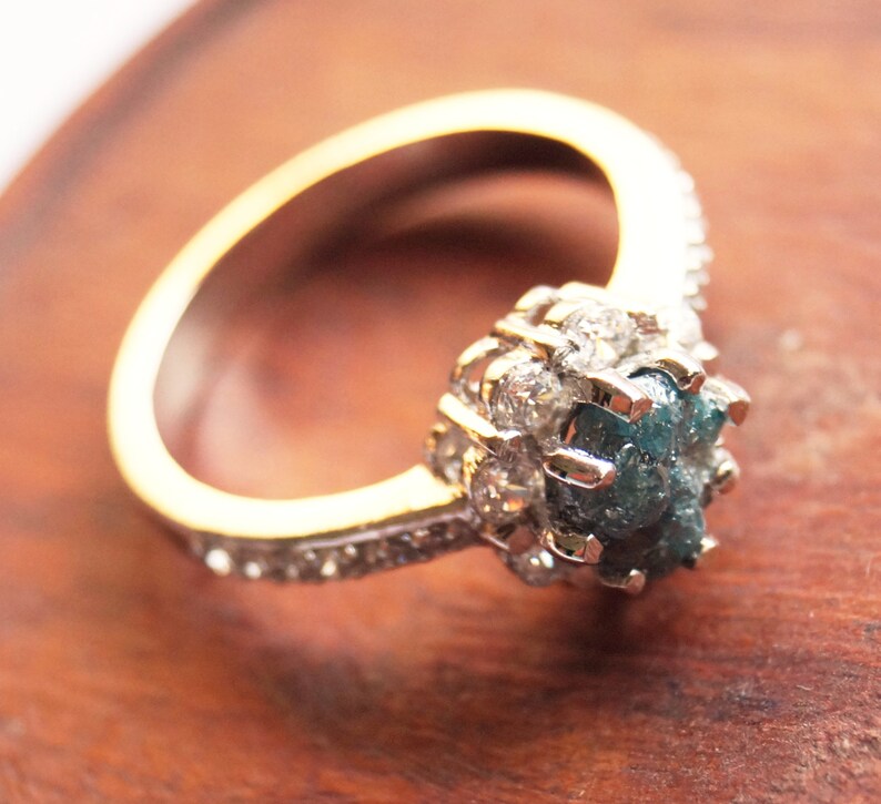 May include: A gold ring with a blue and gray rough diamond set in a halo of smaller diamonds.