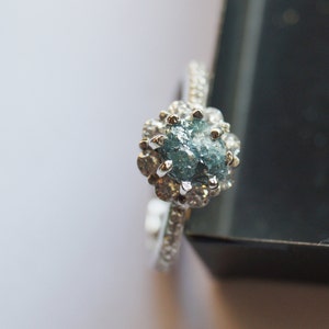 May include: A silver ring with a blue rough diamond set in a halo of smaller diamonds.
