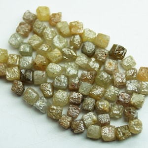 May include: A collection of small, rough, and faceted diamonds in various shades of yellow and brown. The diamonds are scattered on a white surface.