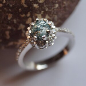 May include: A silver ring with a blue and gray rough diamond set in a halo of smaller diamonds.