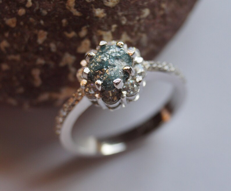 May include: A silver ring with a blue and gray rough diamond set in a halo of smaller diamonds.
