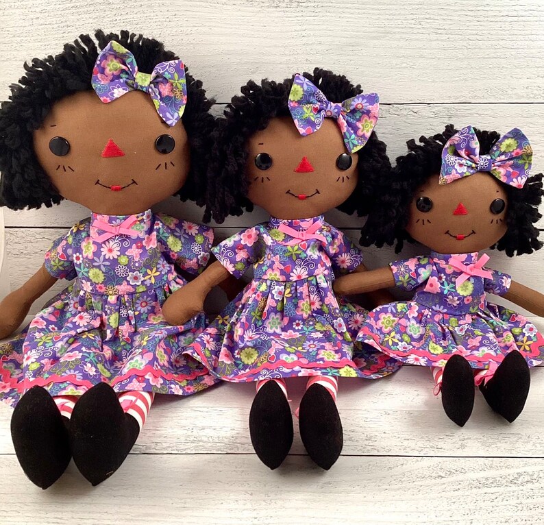Raggedy Ann style doll dressed in floral lavender dress and hair bow. 
She has medium brown skin tone with black yarn hair.
Recommended for ages 3+
Sizes:
Small 13 inches
Medium 16 inches
Large 20 inches