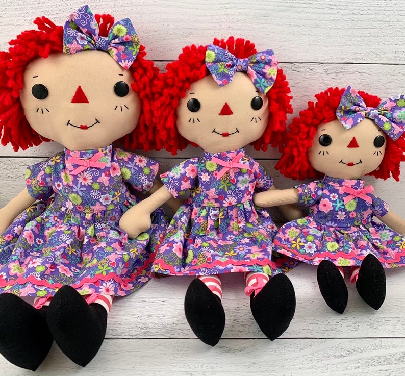 Raggedy Ann style doll is dressed in a removable floral light purple dress with matching hair bow. 
She has light tan skin tone with red hair. Recommended for ages 3 and up.
Doll Sizes:
Small 13 inches
Medium 16 inches
Large 20 inches