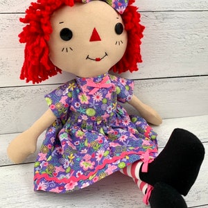 Raggedy Ann style doll is dressed in a removable floral light purple dress with matching hair bow. 
She has light tan skin tone with red hair. Recommended for ages 3 and up.
Doll Sizes:
Small 13 inches
Medium 16 inches
Large 20 inches