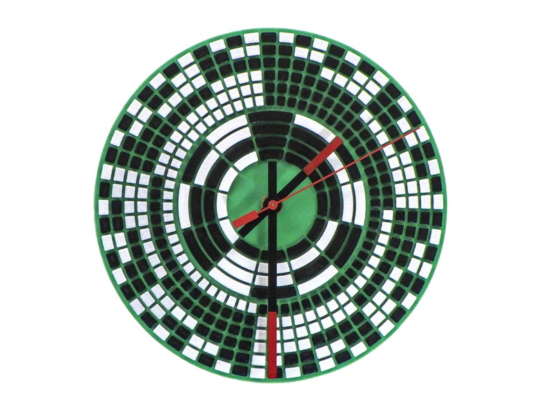 以下が含まれることがあります： 緑、黒、白の幾何学模様が施された丸い壁掛け時計。時計の文字盤には、同心円と正方形が並んでいます。時計の針は赤色で、時針と分針は黒色です。