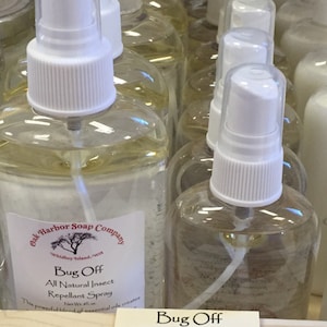 May include: Clear spray bottles with white spray nozzles are arranged in rows. The bottles contain a yellow liquid and are labeled "Bug Off" insect repellent. A sign lists sizes: 4 oz, 8 oz, and 16 oz.