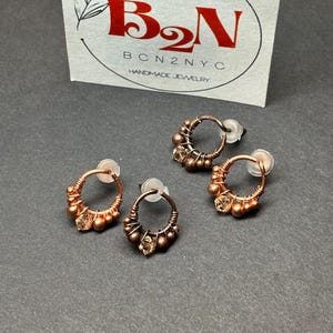 May include: Three pairs of copper wire earrings with small, clear beads. The earrings are handmade and have a simple, elegant design.