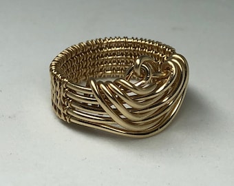 May include: A gold wire ring with a woven design. The ring is made of multiple strands of wire that are woven together to create a unique and intricate pattern.