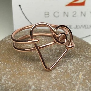 May include: A rose gold wire ring with a heart design. The heart is made of two wires, one wrapped around the other.