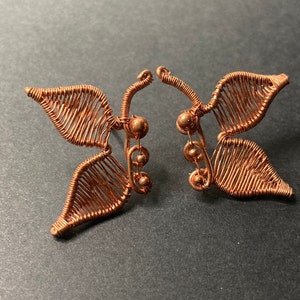May include: A pair of copper wire butterfly earrings with small copper beads. The butterflies have a delicate, intricate design.