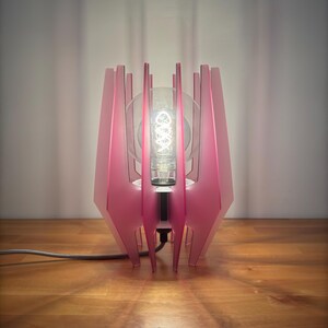 May include: A pink table lamp with a geometric design and a clear glass globe light bulb.