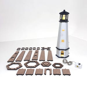 May include: A lighthouse model kit featuring a fully assembled, illuminated white and black tower alongside various unassembled flat wooden pieces, including hexagonal bases, rectangular wall panels, and a small battery-operated light string.
