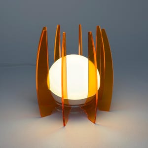 May include: Orange acrylic table lamp with a white globe light. The lamp has a geometric design with multiple thin, curved panels.