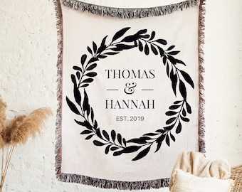 May include: A white throw blanket with a black wreath design and the text "Thomas & Hannah EST. 2019".