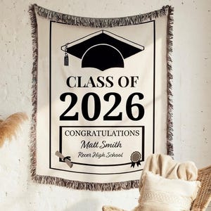 May include: A cream-colored graduation tapestry with a black border, featuring a graduation cap graphic and the text "CLASS OF 2026." Below, it reads "CONGRATULATIONS Matt Smith Recer High School."