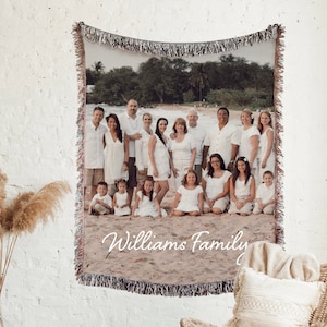 May include: A woven tapestry featuring a family photo of a large group of people in white clothing standing on a beach. The tapestry has a fringe border and the text "Williams Family" is printed at the bottom.