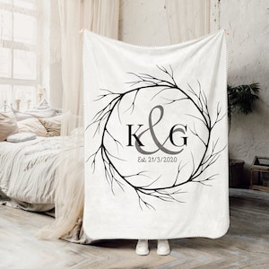 May include: White fleece throw blanket with a black and gray monogram design. The monogram features the letters "K&G" inside a wreath of branches. The text "Est. 21/3/2020" is below the monogram.