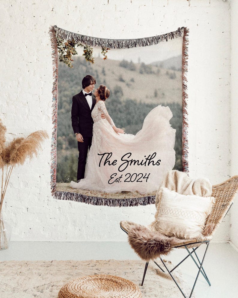May include: Woven tapestry featuring a wedding photo of a couple in formal attire, set against a mountain backdrop. The tapestry includes the text "The Smiths Est. 2024" in elegant script, with fringed edges.