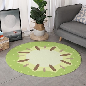 May include: A round green and brown rug with a kiwi fruit design. The rug has a light green background with white dots and a brown kiwi fruit in the center. The kiwi fruit has a light green center and brown seeds.