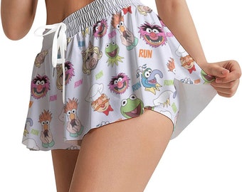 May include: White running shorts with a colorful print of characters from the Muppets. The print includes characters like Cookie Monster, Miss Piggy, and Animal. The shorts have a white elastic waistband and a white drawstring.
