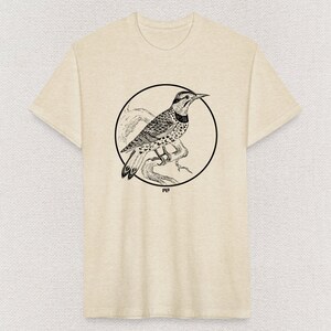 May include: A beige t-shirt with a black and white illustration of a bird in a circle. The bird is perched on a branch and has a spotted pattern. The text "WF" is below the circle.