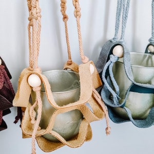 May include: Three macrame plant hangers with wooden beads. The hangers are made of brown, beige, and gray rope. Each hanger has a metal pot attached to it.