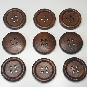 May include: Nine round, dark brown wooden buttons with four holes each. The buttons are arranged in a three-by-three grid, showcasing their uniform size and design. The buttons have a slightly textured surface.