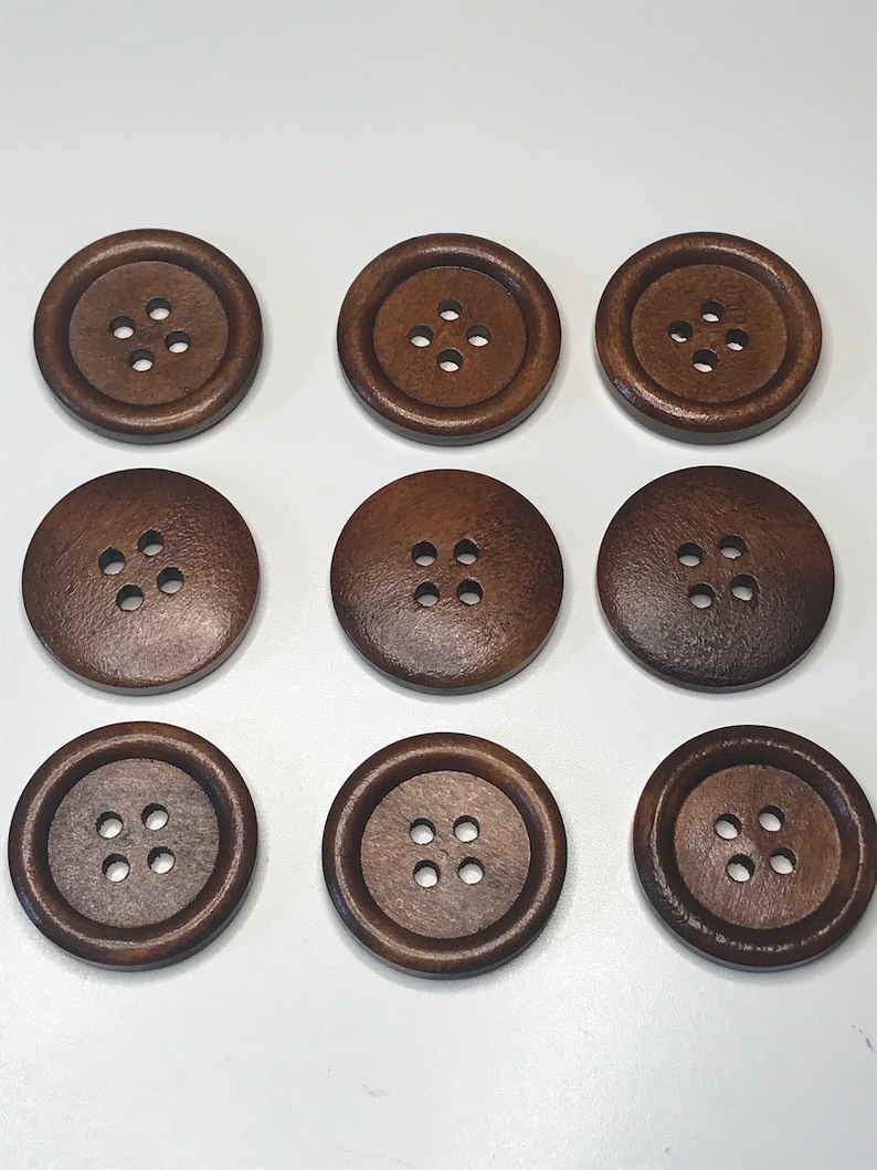 May include: Nine round, dark brown wooden buttons with four holes each. The buttons are arranged in a three-by-three grid, showcasing their uniform size and design. The buttons have a slightly textured surface.
