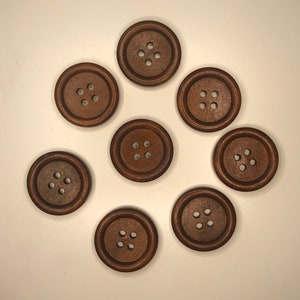 May include: A collection of eight round, dark brown wooden buttons with four holes each. The buttons are arranged in a circular pattern against a white background. These buttons are suitable for sewing and craft projects.
