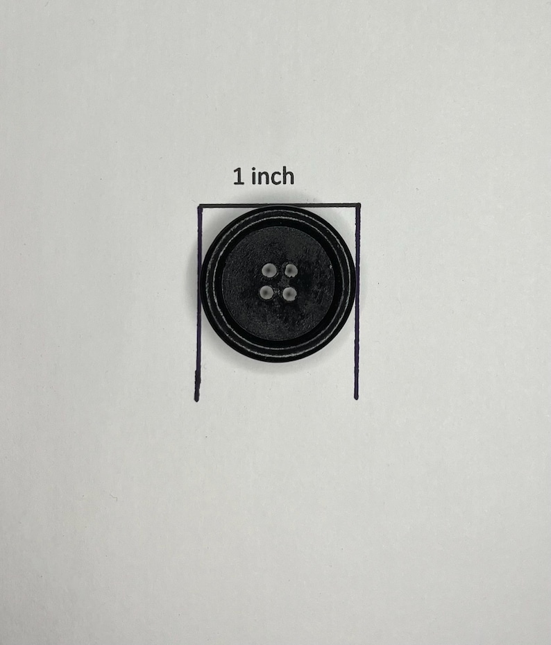 May include: A black button with four holes, approximately 1 inch in diameter, is shown within a drawn square. The button has a ridged outer edge. The text "1 inch" is above the square.