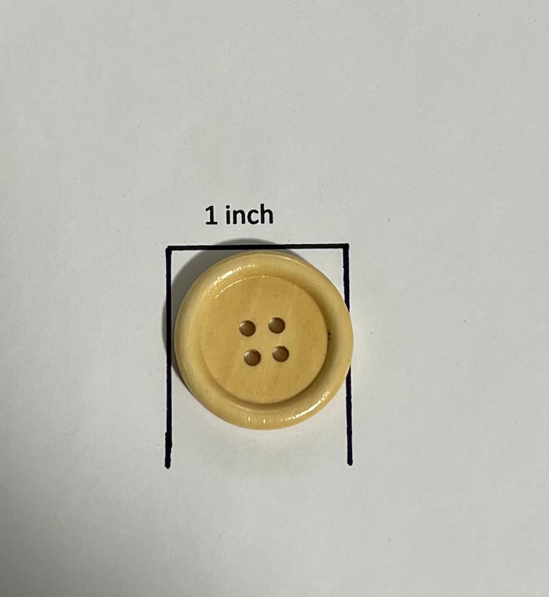May include: A light beige button with four holes, approximately 1 inch in diameter, is shown on a white background. The button has a slightly raised outer rim and a smooth, glossy finish.