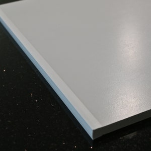 May include: Close-up of a white, smooth, rectangular surface with a slightly raised edge. The surface is reflecting light, creating a subtle sheen.