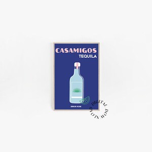 Puede incluir: Una impresión artística enmarcada con un fondo azul oscuro, que muestra las palabras "CASAMIGOS TEQUILA" en rosa. Presenta una botella de tequila azul claro con una tapa rosa y una rodaja de lima. El texto "ERROR ROSE" está en la parte inferior.
