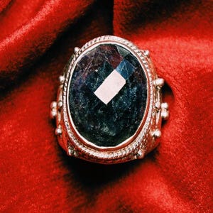 May include: A silver ring with a large, oval-shaped, dark blue gemstone set in a silver bezel. The ring has a decorative, textured band with small silver beads.
