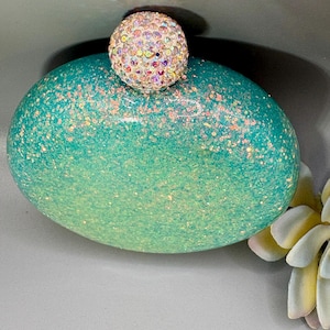 This is a palm sized, round stainless steel hip flask, with a teal/turquoise glitter finish and rhinestone knob/top.