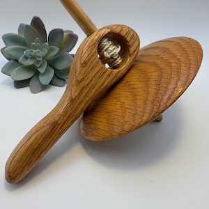 May include: A wooden spinning top with a rounded base and a handle. The top is made of light brown wood with visible grain. A string is visible in the center of the top. The top is a classic toy.
