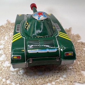 May include: Vintage green toy tank with a red and silver turret. The tank features yellow and silver accents, and the number "721" is visible on the turret. A red star is on the turret. A classic collectible toy.