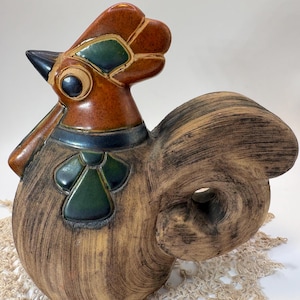 May include: A ceramic rooster figurine featuring a textured, light brown wood-grain finish on the body and tail. The head is glazed in a glossy reddish-brown with dark green accents on the comb and neck, and a black beak and eye detail.