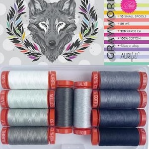 May include: A clear plastic case containing ten spools of Aurifil cotton thread in various shades of gray. The case is labeled "GRAYWORK" and features a detailed illustration of a wolf's head. Each spool contains 220 yards of thread.