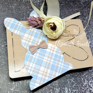 May include: A blue and brown plaid bunny cutout with a brown bow tie. The bunny is on a brown cardstock background with the text "DESIGNED BY Elizabeth Terrell".