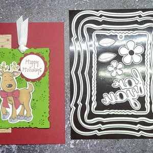 May include: A red card with a green tag attached. The tag has a cartoon reindeer with a red bow and the text "Happy Holidays". The card is next to a black and white die-cut frame with multiple layers.