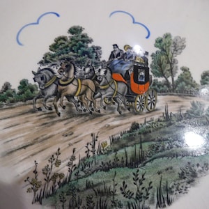 May include: A vintage style plate with a hand-painted scene of a horse-drawn carriage traveling through a countryside landscape. The carriage is red with black accents and is pulled by three horses. The scene is painted in shades of brown, green, and blue.