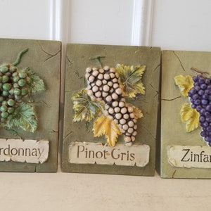 May include: Three decorative wall plaques with grape clusters and the names of wine varietals: Chardonnay, Pinot Gris, and Zinfandel.