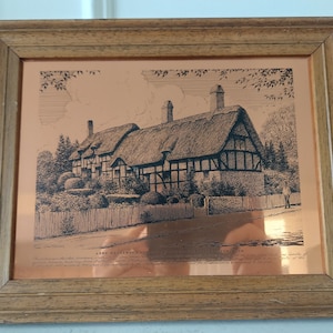 May include: A framed copper etching of a thatched-roof cottage with a wooden frame. The etching is titled "Anne Hathaway's Cottage" and includes a description of the cottage.