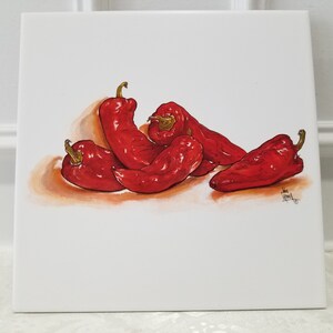 May include: A hand-painted ceramic tile featuring a still life of five red peppers. The peppers are arranged in a cluster, with some overlapping. The tile has a white background and a subtle orange shadow beneath the peppers.