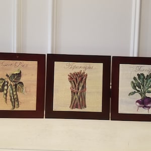 May include: Three framed prints with a rustic background and a vintage style. Each print features a different vegetable: sweet peas, asparagus, and turnips. The frames are dark brown wood.