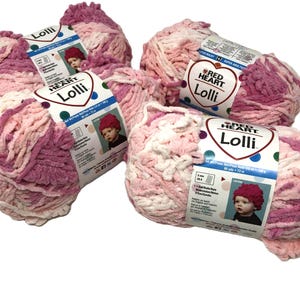 May include: Three skeins of Red Heart Lolli super bulky yarn in a variegated pink, white, and magenta colorway. Each skein features a white paper label with the brand name, a photo of a child wearing a hat, and technical knitting specifications.