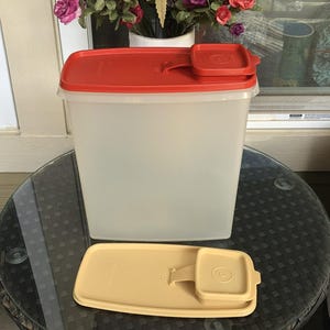 May include: A rectangular, translucent plastic food storage container with a bright red lid featuring a small hinged pour spout. An additional, separate beige lid of the same rectangular design with a hinged pour spout is placed in front.