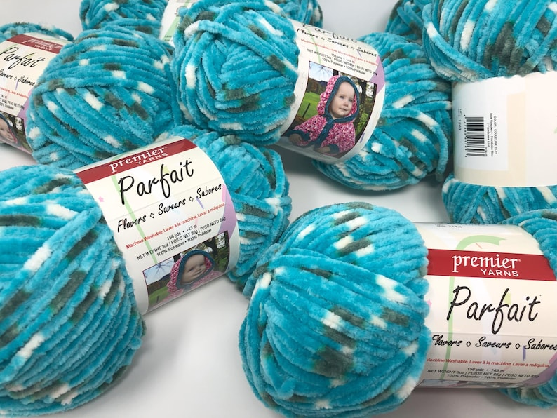May include: Multiple skeins of Premier Yarns Parfait yarn in a variegated turquoise, white, and dark gray colorway. Each skein features a paper label with the brand name, product name, and a photo of a child wearing a hooded garment.