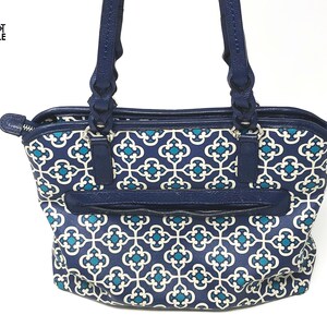 May include: A navy blue tote bag with a white and teal geometric pattern. The bag has navy blue handles and trim, with a zippered pocket on the front. The bag has the text "Knot Simple Boutique" in the upper left corner.